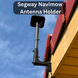 Puede incluir: Un soporte de antena Segway Navimow negro está montado en una estructura de madera con un techo rojo. El soporte de la antena tiene una parte superior cuadrada y un poste vertical largo. El texto "Segway Navimow Antenna Holder" se muestra en la parte superior de la imagen.
