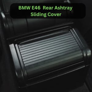 May include: Black rear ashtray sliding cover for a BMW E46. The cover is rectangular with a ridged, sliding design. The text "BMW E46 Rear Ashtray Sliding Cover" is displayed in green text on a black background.