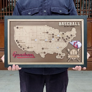 May include: A wooden baseball map of the USA, featuring team logos and the word "Baseball". The map includes the Cleveland Guardians logo and a baseball bat and ball emblem. The frame is dark green. The map is in a wooden frame.