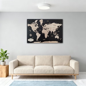 May include: A large, black wooden world map with countries labeled in white. The map is mounted on a wall above a beige sofa. A compass rose and text are visible on the lower left corner. The map is a decorative piece.