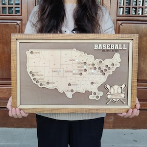 Op de afbeelding: Houten honkbalkaart van de Verenigde Staten met een lichtbruine lijst. De kaart toont honkballen die de locaties van de Major League markeren. De woorden "BASEBALL MAJOR LEAGUE" staan bovenaan. Een klein bordje onderaan zegt "MappaePilot MLB Stadium Map".