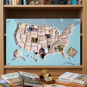 May include: A rectangular light blue wall map of the United States featuring laser-cut wooden state outlines. Several states contain personal photographs. A wooden compass rose in the bottom right corner displays the text Patrick & Fiona USA Travel Map.