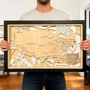 May include: A framed wooden map of the USA, featuring laser-cut football stadium details. The map includes player silhouettes and a football. The text reads "Johnson Family NFL Stadium Tour".