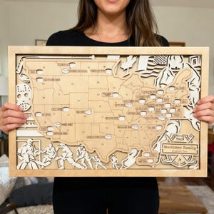 May include: Wooden hockey-themed map of the United States with laser-cut details. The map features hockey-related imagery, including a hockey mask, players, and a hockey puck. The map is framed and includes the text "Mortimer Family".