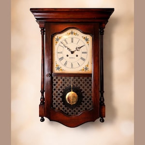 May include: A dark wood wall clock with a cream-colored face featuring black Roman numerals and delicate floral accents. The clock has a pendulum and a decorative lower panel. The clock is approximately 24 inches tall.