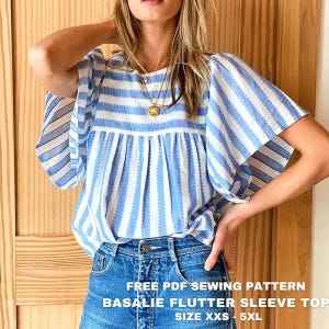 Op de afbeelding: Een blauw en wit gestreepte top met vlindermouwen en een ronde halslijn. Het kledingstuk heeft een geplooid lijfje en verticale strepen. De tekst op de afbeelding luidt: FREE PDF SEWING PATTERN BASALIE FLUTTER SLEEVE TOP SIZE XXS - 5XL.