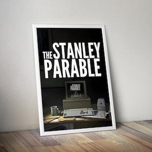 May include: Framed poster with the words "THE STANLEY PARABLE" in white. The image shows a computer setup with the game's title on the screen. A mug, keyboard, and office items are on the desk. The poster is in a white frame.