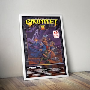 Könnte beinhalten: Ein gerahmtes Poster für das Videospiel "Gauntlet II". Das Kunstwerk zeigt eine Fantasieszene mit Charakteren, die Waffen schwingen, einem Zauberer und Blitzen. Der Spieletitel ist in goldfarbenen Buchstaben gehalten, mit dem Text "GAUNTLET II" und "4 PLAYER GAME."