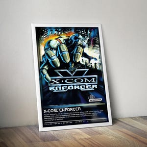 Pode incluir: Pôster emoldurado do videogame "X-COM: Enforcer". A arte apresenta uma mão robótica estendida, com uma paisagem urbana e explosões ao fundo. O título do jogo é exibido de forma proeminente.