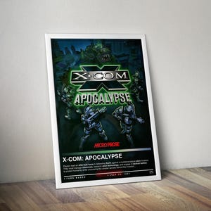 May include: A framed poster for the video game X-COM: Apocalypse. The artwork features soldiers in futuristic armour, a green alien, and the game's logo. The poster has the text "X-COM Apocalypse" and "Micro Prose". The poster is leaning against a wooden surface.
