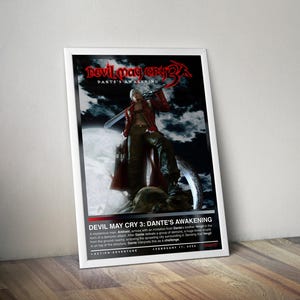 May include: Framed poster for "Devil May Cry 3: Dante's Awakening." The image shows a character in a red coat with a sword, set against a dark background. The game's title is at the top, with a description below. The poster is propped against a wooden floor.