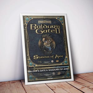 May include: A framed poster for the video game Baldur's Gate II: Shadows of Amn. The poster features a dark blue background with gold lettering and accents. The game's title and a character illustration are prominently displayed. The poster is set against a wooden surface.