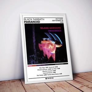 May include: A framed poster for Black Sabbath's album "Paranoid." The poster features the album title and band name in white text. The album art shows a blurred figure in a forest. The tracklist is listed at the bottom.