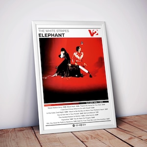 May include: Framed poster featuring The White Stripes' album "Elephant." The artwork showcases two figures against a red backdrop. The poster includes the album title, tracklist, and release date. The frame is white, and the poster is displayed on a wooden surface.