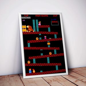 May include: A framed print of the classic arcade game Donkey Kong. The image features the game's iconic characters and level design, with a high score display and the text "1UP 000300". The print is set against a white wall and rests on a wooden surface.