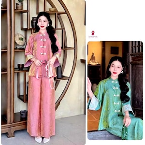 May include: A pink traditional two-piece outfit with a mandarin collar and frog closures. The outfit includes a long-sleeved top and wide-leg pants. The outfit is made of a textured fabric. The image also shows a green version of the outfit.