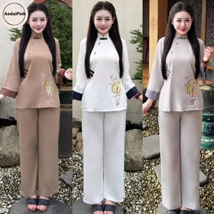 May include: Three sets of traditional Vietnamese Ao Dai outfits. The outfits include a long-sleeved top with a mandarin collar and embroidered details, paired with matching wide-leg pants. The colors are tan, white, and light gray.