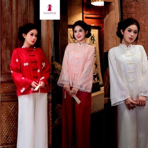 May include: Three women wearing traditional Asian-style blouses and pants. The blouses are red, pink, and white, with floral embroidery and frog closures. The pants are white and red. The brand name "AodailPink" is visible in the top left corner.