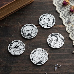May include: Five circular metal pins featuring black and white illustrations of various characters. Each pin displays a unique character design enclosed in a circular border with the word yes printed in a stylized font along the top edge.
