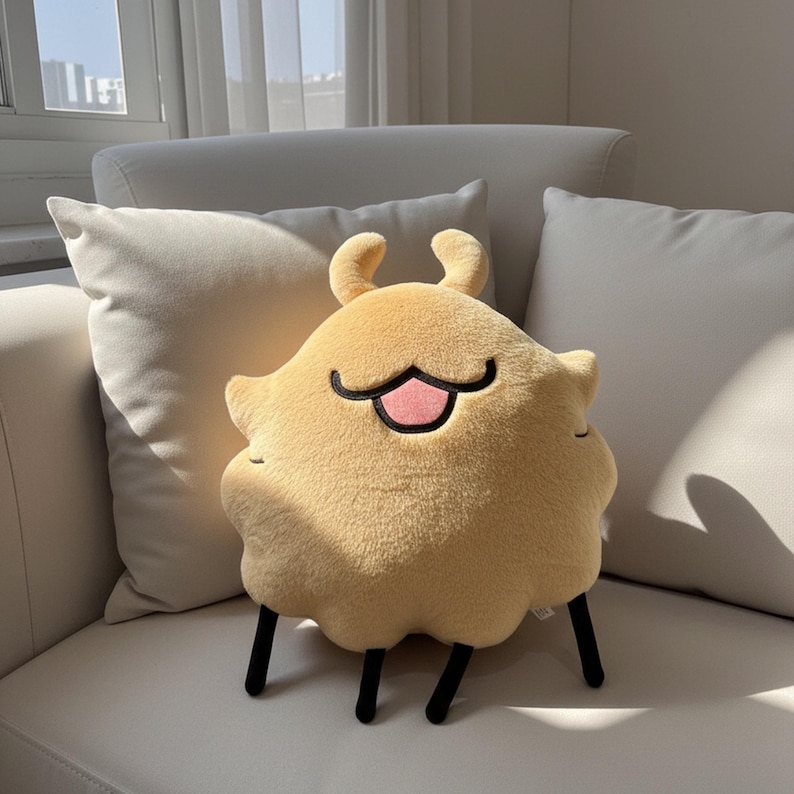 May include: A plush, yellow creature-shaped pillow with a smiling face and black legs. The pillow has a rounded body with two small, curved antennae. The mouth is a black line with a pink tongue. The pillow is on a white couch.