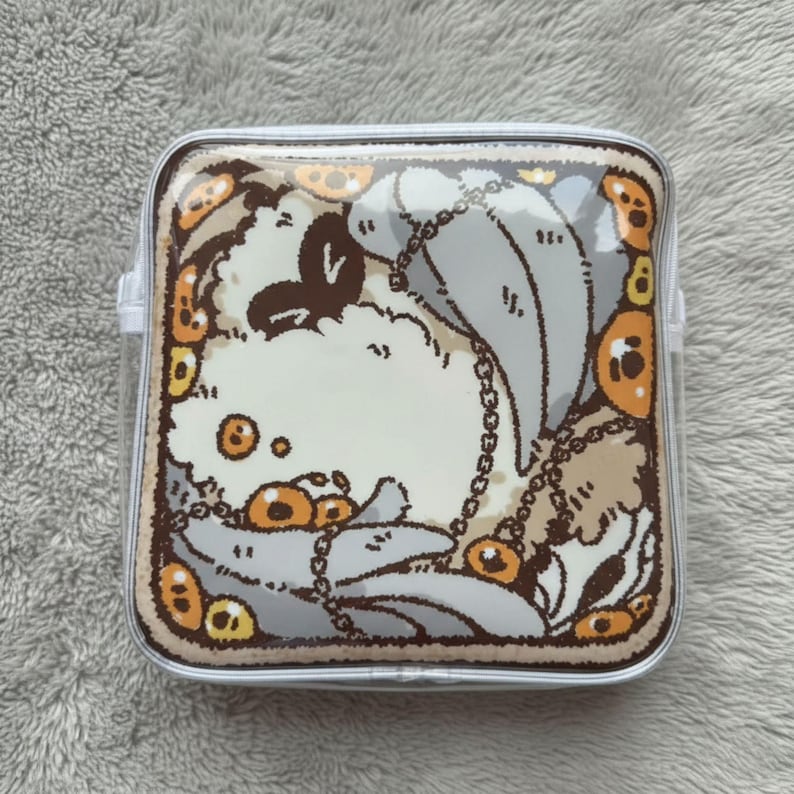 May include: Square, clear cosmetic bag with a cartoon illustration. The design features a white, fluffy creature with gray accents, a chain, and orange circular details. The bag has a clear plastic body and a silver trim.