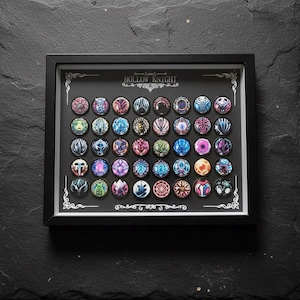 May include: A framed display featuring a collection of colorful, circular pins. Each pin showcases a unique design with intricate patterns and vibrant hues, set against a black background. The frame includes the text "Hollow Knight".