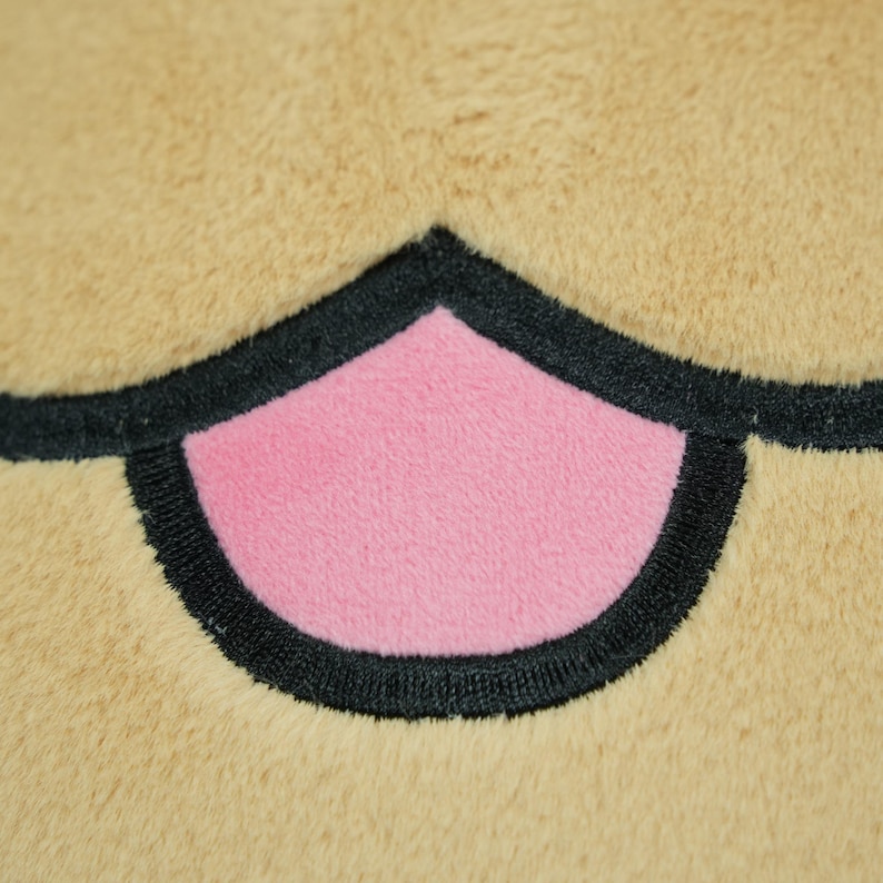 May include: Close-up of a plush toy's mouth, featuring a pink center and black outline against a tan background. The plush material has a soft, textured appearance, suggesting a cuddly toy.