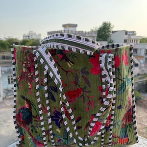 Könnte beinhalten: Grüne Cord-Tragetasche mit einem Blumenmuster in Rot, Lila und Gelb. Die Tasche hat einen gestreiften Griff und Besatz. Die Tasche ist zum Tragen von Gegenständen konzipiert.