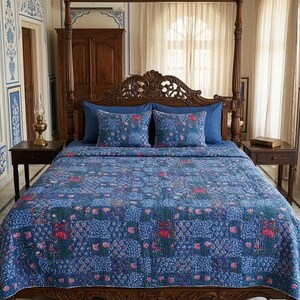 May include: A dark blue bedspread with a floral pattern, featuring red and pink accents, covers a wooden bed frame. Two matching throw pillows rest against a dark blue headboard. The room has a vintage aesthetic.