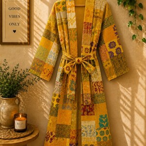 May include: A long-sleeved robe featuring a patchwork design with various yellow, orange, and green floral and geometric patterns. The garment includes a matching fabric tie belt at the waist and a wide collar, constructed from quilted fabric.