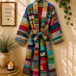 May include: A long-sleeved robe featuring a patchwork design composed of various colorful fabric strips with diverse patterns, including floral, geometric, and animal motifs. The robe includes a matching tie belt at the waist and a shawl collar.