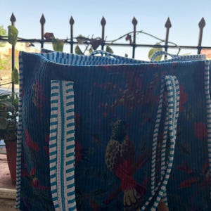 May include: A blue corduroy tote bag with a bird and floral pattern. The bag has striped handles and trim in white and light blue. The bag is open, revealing a striped interior.