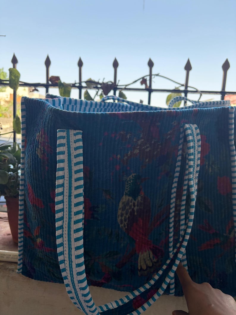 May include: A blue corduroy tote bag with a bird and floral pattern. The bag has striped handles and trim in white and light blue. The bag is open, revealing a striped interior.