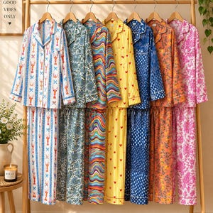 Puede incluir: Siete conjuntos de camisas de pijama de manga larga con botones y pantalones a juego colgados en un perchero de madera. Los estampados incluyen langostas sobre blanco, flores azules, líneas onduladas multicolores, corazones rojos sobre amarillo, puntos azules, flores naranjas y flores rosas.