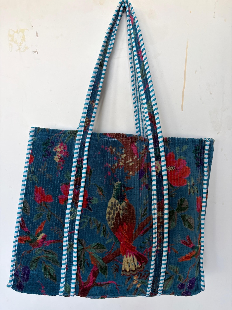 May include: Teal tote bag with a floral and bird pattern. The bag features a corduroy texture and white and teal striped handles. The design includes red flowers and a detailed bird illustration.
