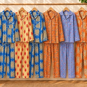 Könnte beinhalten: Sechs Sets aus langärmeligen, geknöpften Schlafanzugoberteilen und passenden Hosen, die an einem Holzständer hängen. Die Muster umfassen Blau mit Tigermotiven, Gelb mit roten Hummern, Orange mit Blumenranken und blaue Streifen mit kleinen roten Herzen.