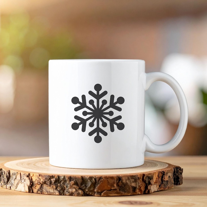 Op de afbeelding: Witte keramische mok met een zwart sneeuwvlokontwerp. De sneeuwvlok is gecentreerd en heeft een gedetailleerd, symmetrisch patroon. De mok heeft een gebogen oor en staat op een houten onderzetter.