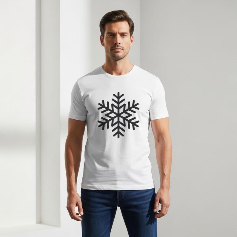 Op de afbeelding: Wit T-shirt met een zwart sneeuwvlokontwerp. Het T-shirt heeft korte mouwen en wordt gecombineerd met een blauwe jeans. Het sneeuwvlokontwerp is een winterthema.