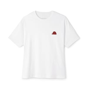 Puede incluir: Camiseta blanca con un pequeño diseño de cuadros rojos y negros en la parte superior derecha del pecho. La camiseta tiene mangas cortas y cuello redondo. El nombre de la marca está impreso en el cuello.