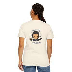 Peut inclure: T-shirt de couleur crème avec un motif graphique au dos. Le motif représente un personnage de dessin animé avec le texte "WHATEVER" au-dessus et "I'D RATHER BE AT THE GAME" en dessous. Comprend un ballon de foot, des étoiles et des chaussures de foot.