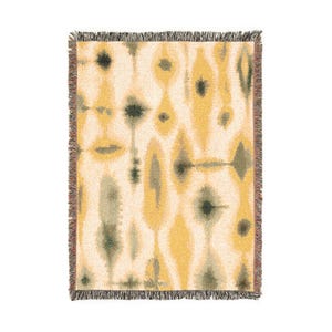 May include: A rectangular woven throw blanket featuring a repeating abstract pattern of elongated yellow and dark gray shapes on a cream-colored background. The blanket is finished with a short, frayed fringe along all four edges of the fabric.