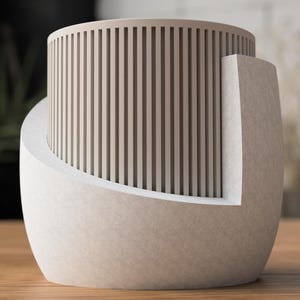 May include: A modern, beige-colored decorative vase with a cylindrical top featuring vertical, narrow slats. The vase has a curved, rounded base and a rectangular side element. The design is minimalist and contemporary, suitable for home decor.