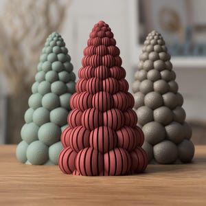 Puede incluir: Tres esculturas cónicas dispuestas en fila. La escultura central es de color rojo oscuro con ranuras verticales en cada segmento esférico. La escultura de la izquierda es verde claro y la de la derecha es gris, ambas con superficie texturizada.