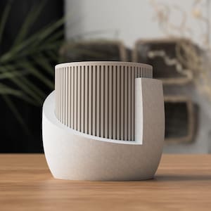 May include: A modern, abstract decorative object. The piece features a cylindrical top with vertical wooden slats, set within a curved, off-white base. The design is minimalist and sculptural, suitable for home decor.