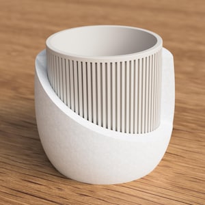 May include: A white, modern-style mug with a unique design. The mug features a cylindrical inner cup with vertical lines, set within a curved, textured outer shell. The design is minimalist and contemporary, suitable for home decor.
