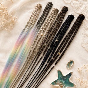 May include: A collection of long hair extensions featuring braided tops and loose, straight ends. The set includes two pastel rainbow-coloured strands, two light brown strands, and two dark brown strands, each accented with small metallic beads.