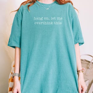 May include: Seafoam green t-shirt with the text "hang on, let me overthink this" in white. The shirt is a solid colour and has short sleeves. The model is 163cm and 54kg and wearing XL.