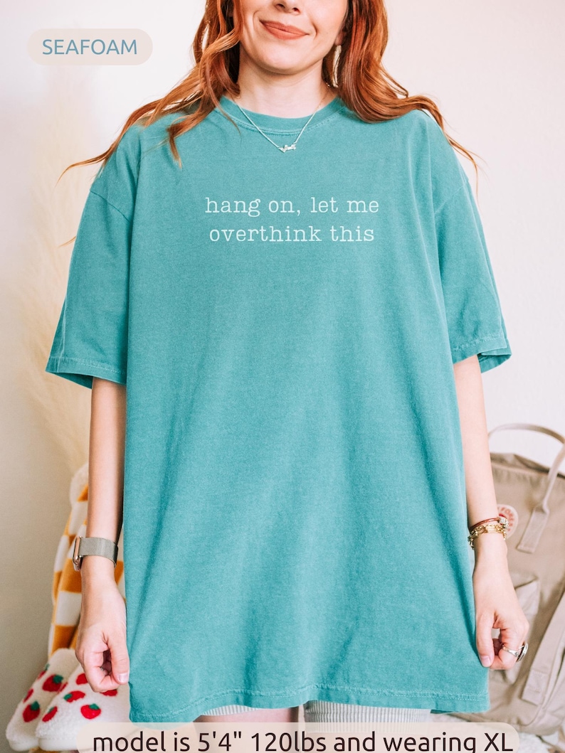 May include: Seafoam green t-shirt with the text "hang on, let me overthink this" in white. The shirt is a solid colour and has short sleeves. The model is 163cm and 54kg and wearing XL.