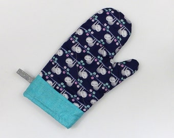 Könnte beinhalten: Ein blauer Topflappen mit einem Muster aus Faultieren, die an Ästen mit rosa Blüten hängen. Der Topflappen hat einen türkisfarbenen Saum.