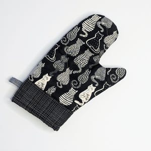 May include: Black oven mitt with a white cat pattern. The mitt is quilted and has a hanging loop.